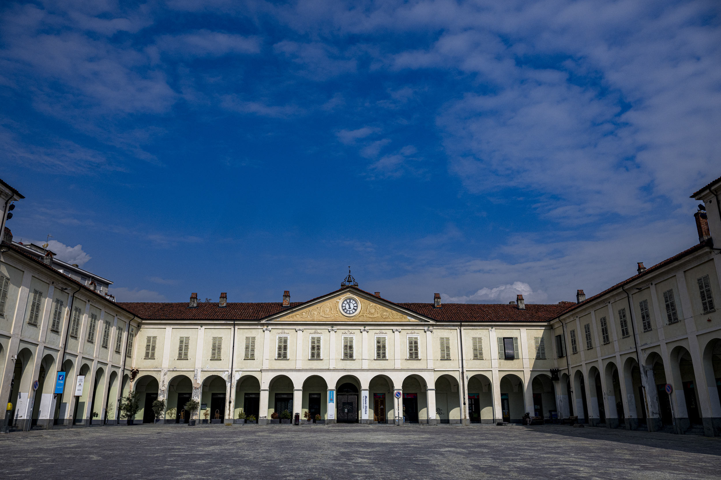 Facciata con orologio e portici nella piazza storica di Ivrea sotto un ampio cielo azzurro