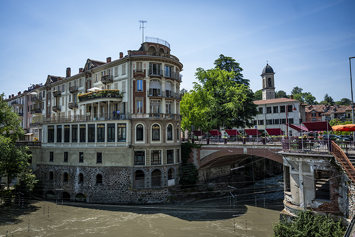 Historic curved riverside building with balconies and terraces beside an arched bridge and bell tower