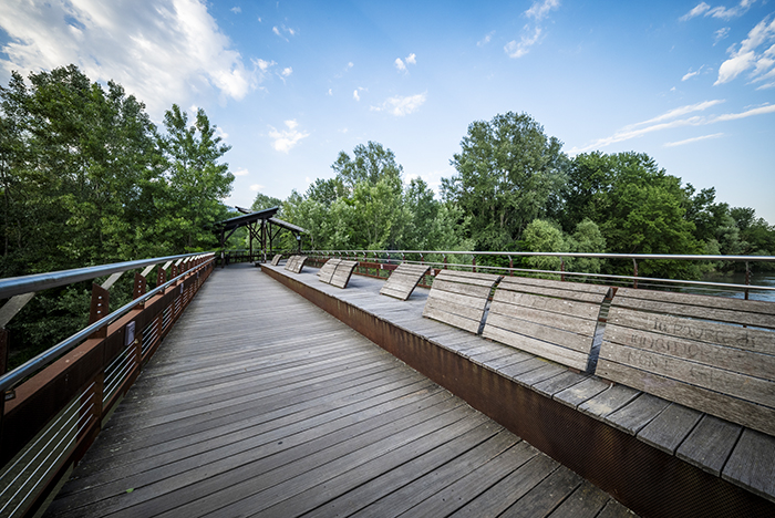 Passerella pedonale in legno con sedute panoramiche sul fiume a Ivrea circondata da alberi