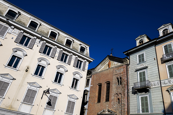Facciata in mattoni di chiesa medievale affiancata da palazzi storici nel centro di Ivrea, cielo terso.