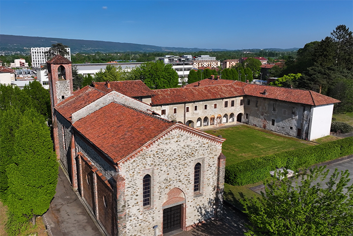 Chiesa con campanile e chiostro con portico e corte erbosa, tetti rossi, nel contesto urbano di Ivrea e colline sullo sfondo